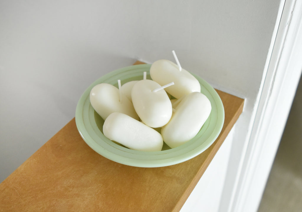 White candles in a green bowl on a wooden surface with a white wall background，韓國設計品牌，天然大豆香氛蠟燭