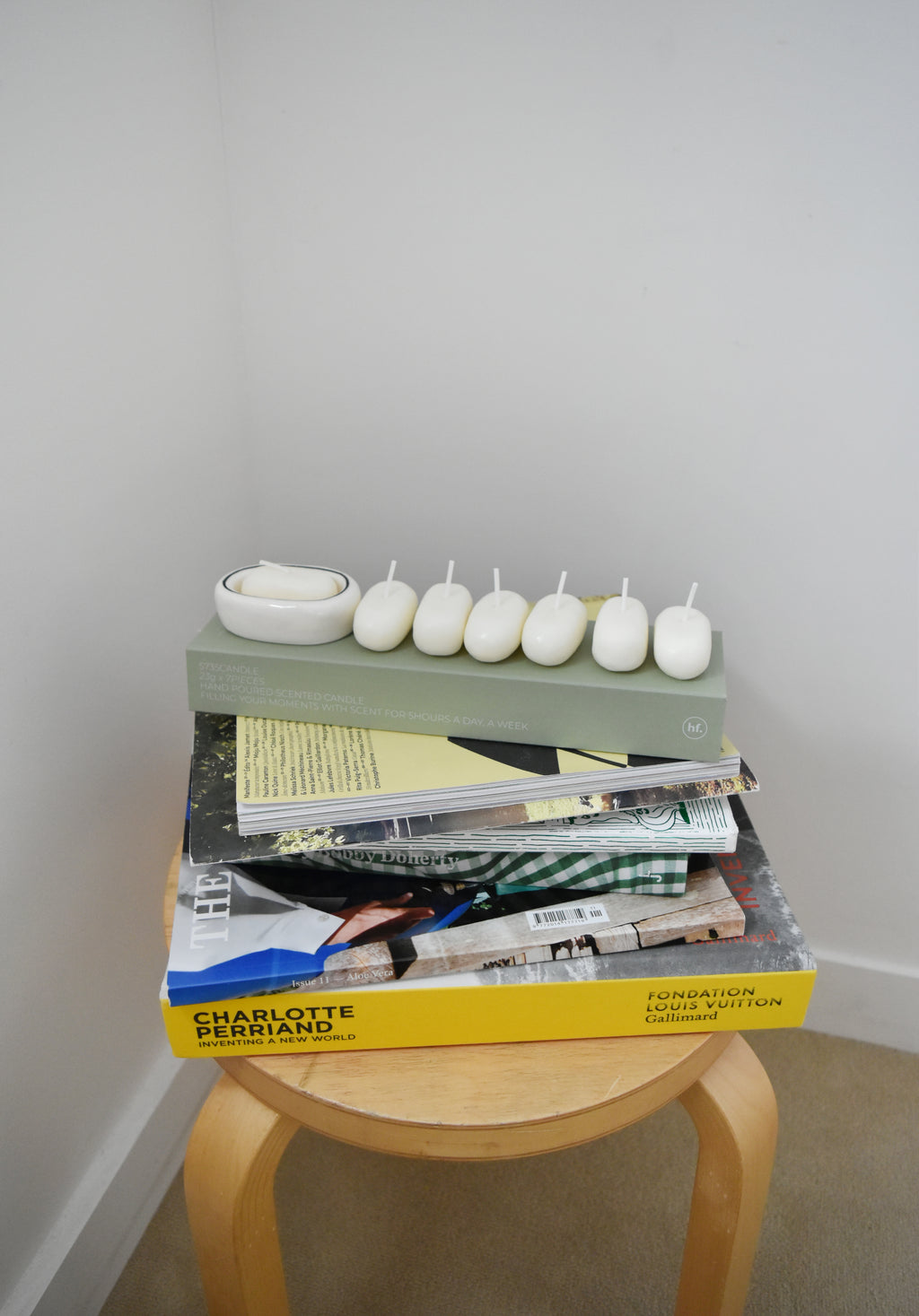 Stack of books with decorative items on a small wooden stool against a plain wall，Honey Flamingo，韓國設計品牌，天然大豆香氛蠟燭