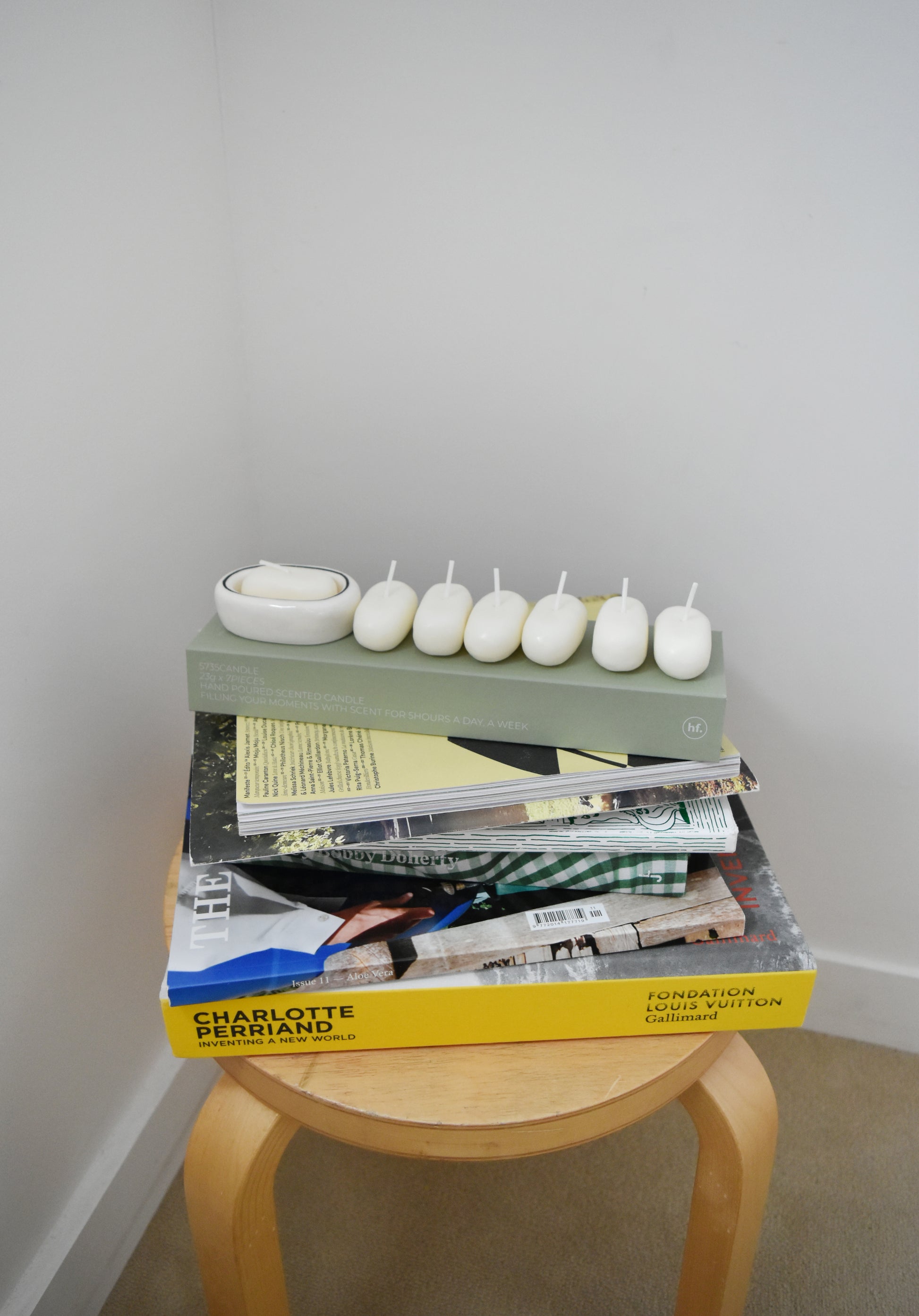 Stack of books with decorative items on a small wooden stool against a plain wall，Honey Flamingo，韓國設計品牌，天然大豆香氛蠟燭