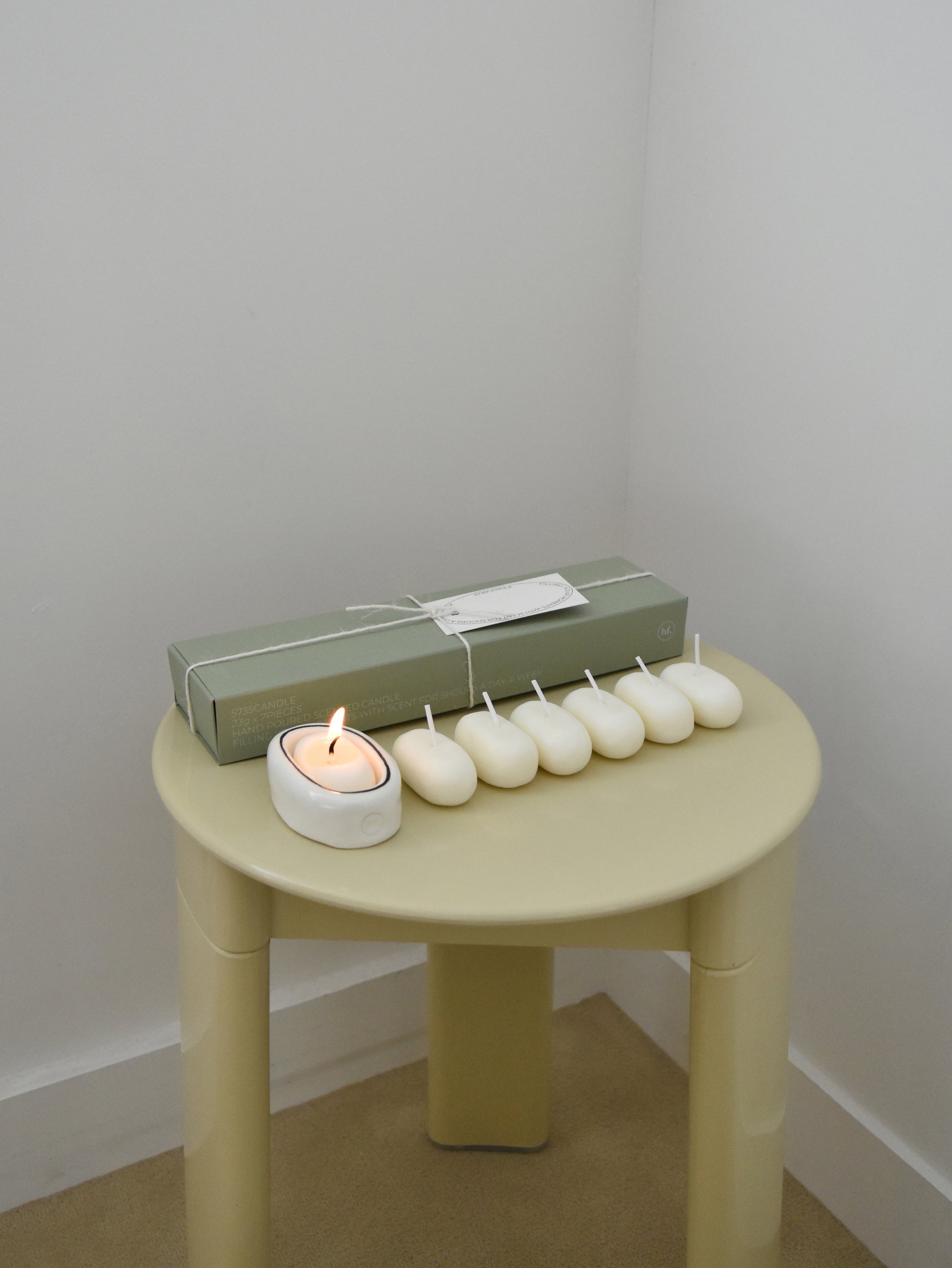 Small round chair with a lit candle, wrapped gift, and small white candles，韓國設計品牌，天然大豆香氛蠟燭