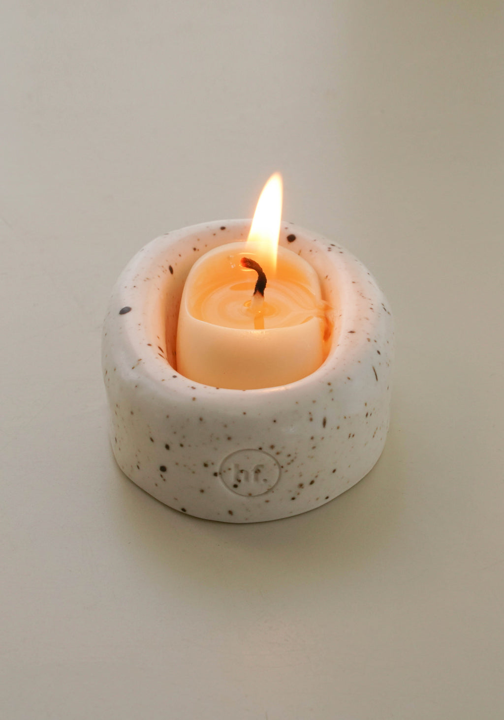 Small speckled ceramic candle holder with a lit candle on a plain background, Honey Flamingo Candle set