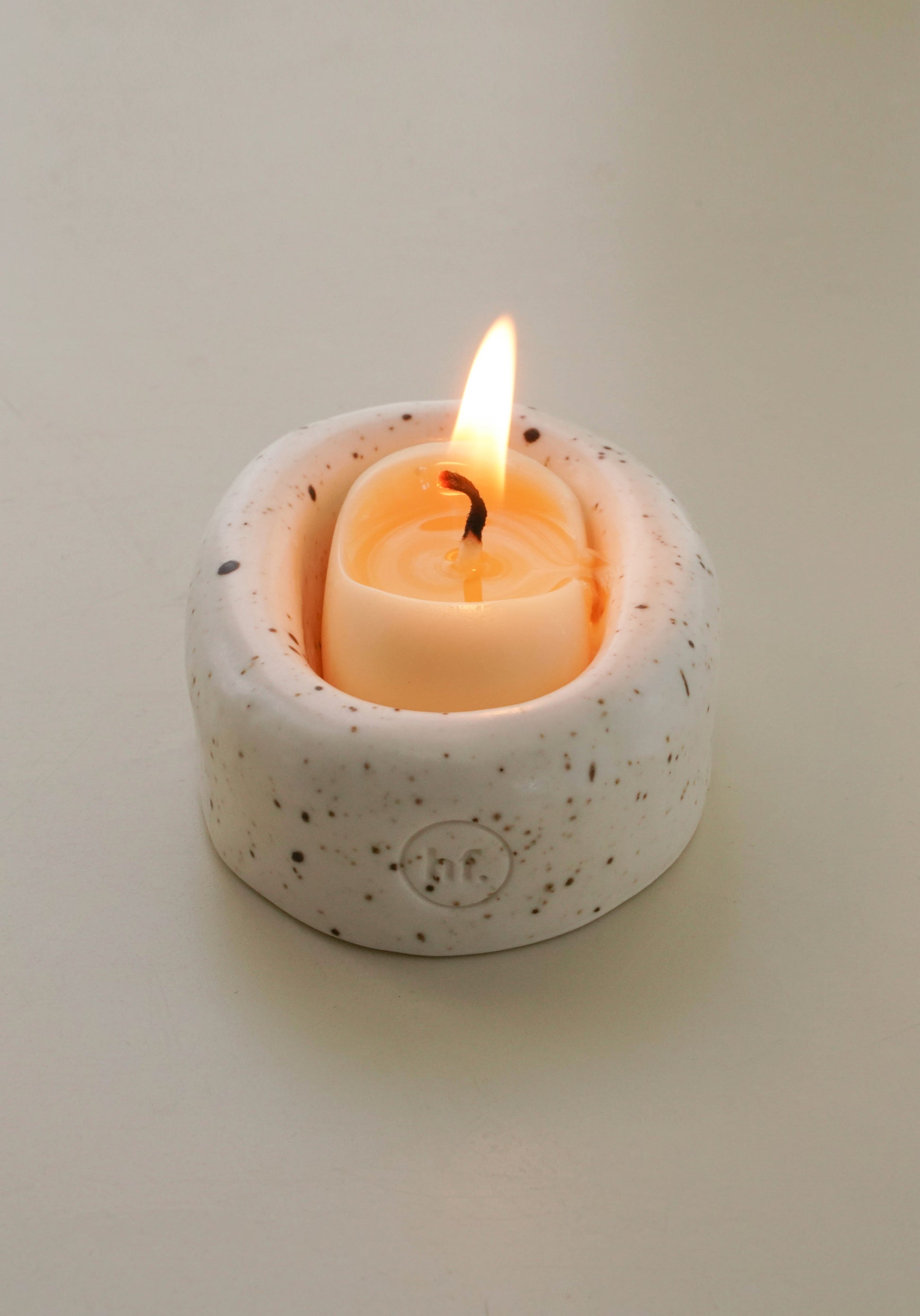 Small speckled ceramic candle holder with a lit candle on a plain background, Honey Flamingo Candle set