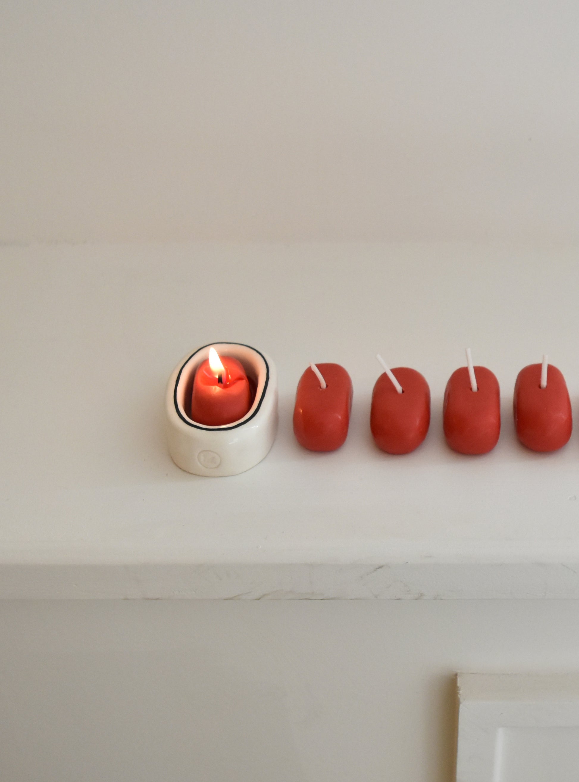Row of red candles with one lit on a white surface，Honey Flamingo，韓國設計品牌，天然大豆香氛蠟燭