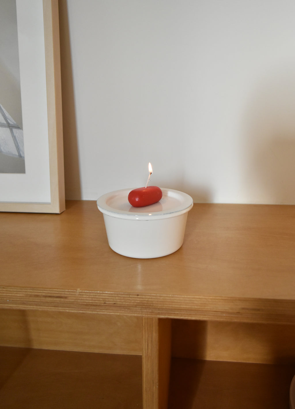 White container with a red object and lit candle on a wooden surface，Honey Flamingo，韓國設計品牌，天然大豆香氛蠟燭