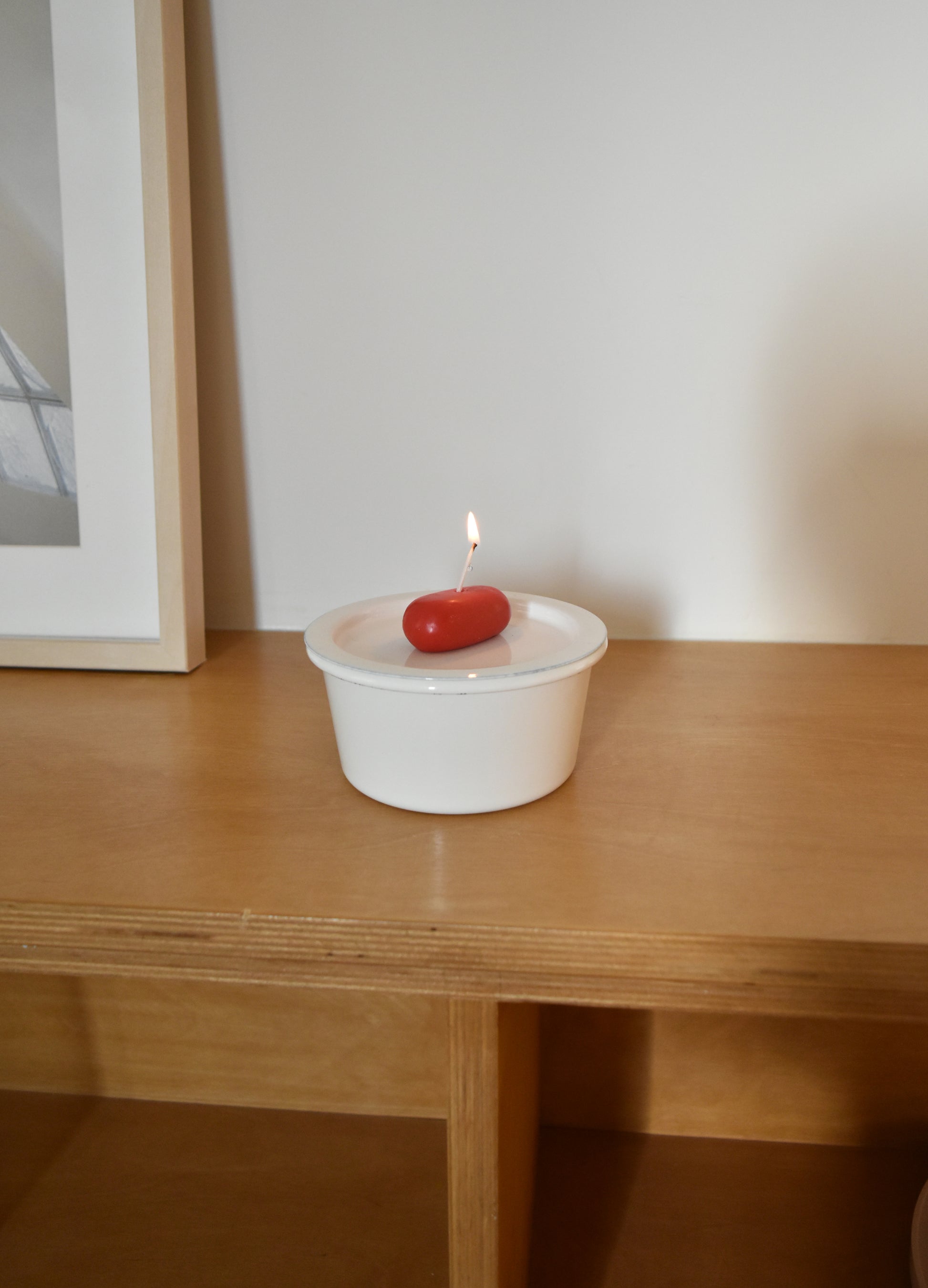 White container with a red object and lit candle on a wooden surface，Honey Flamingo，韓國設計品牌，天然大豆香氛蠟燭