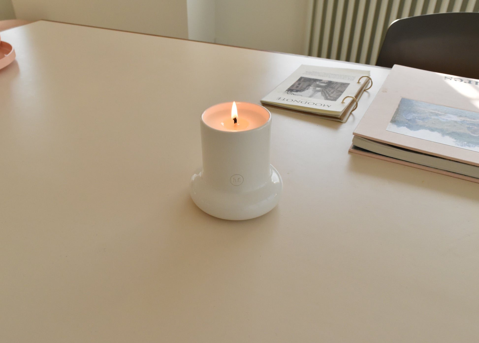Candle in a white holder on a table with books in the background，Honey Flamingo，韓國設計品牌，天然大豆香氛蠟燭