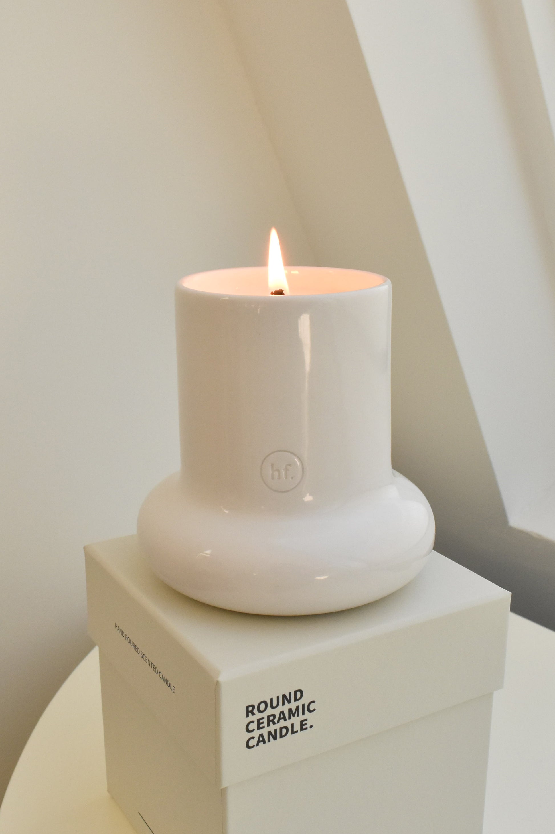 White ceramic candle on a box with 'Round Ceramic Candle' text, lit against a neutral background.，Honey Flamingo，韓國設計品牌，天然大豆香氛蠟燭