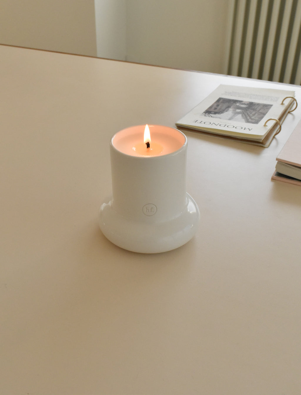 White candle in a holder on a light surface with a blurred background，Honey Flamingo，韓國設計品牌，天然大豆香氛蠟燭