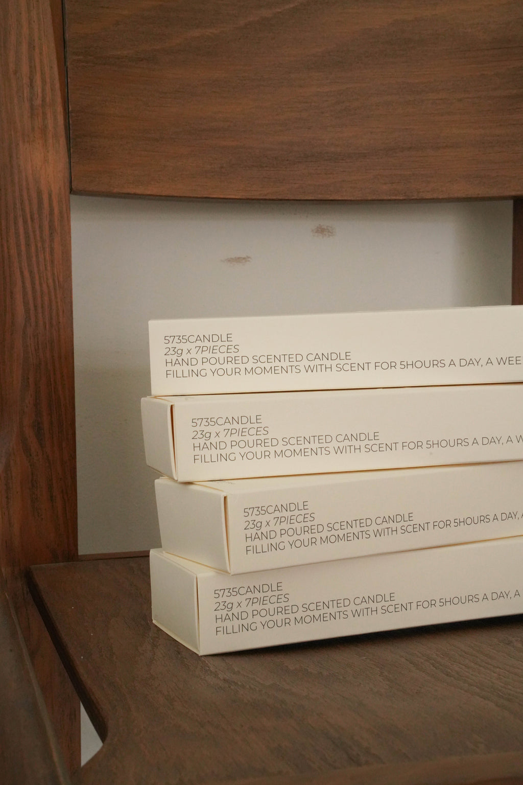 Stack of candle boxes on a wooden surface with a wooden cabinet in the background